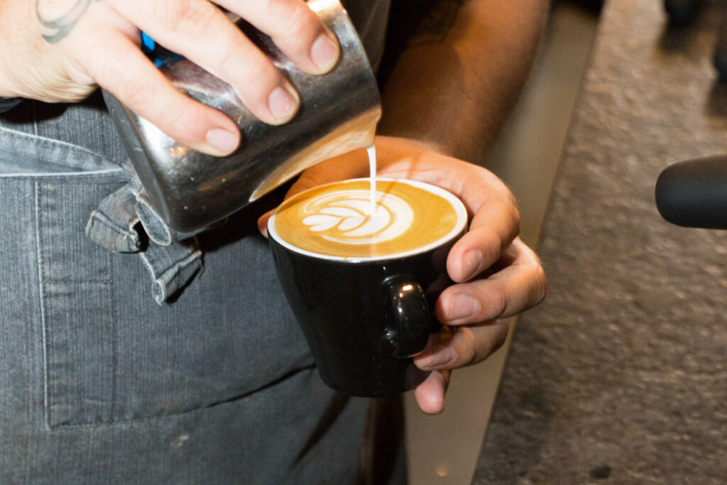 barista pours milk in coffee at honey and harvey